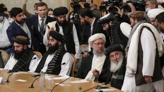 A group of Taliban officials sitting at a conference table with press behind them.