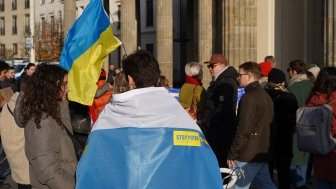 Berlin, Germany - November 13, 2022: Male demonstrator covered with a white-blue-white flag at a rally in solidarity with Ukraine against Russian Imperialism at Brandenburg Gate in Berlin