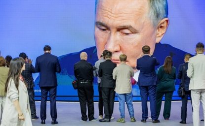 A crowd of people take pictures and watch a largescreen broadcast of President Vladimir Putin. 