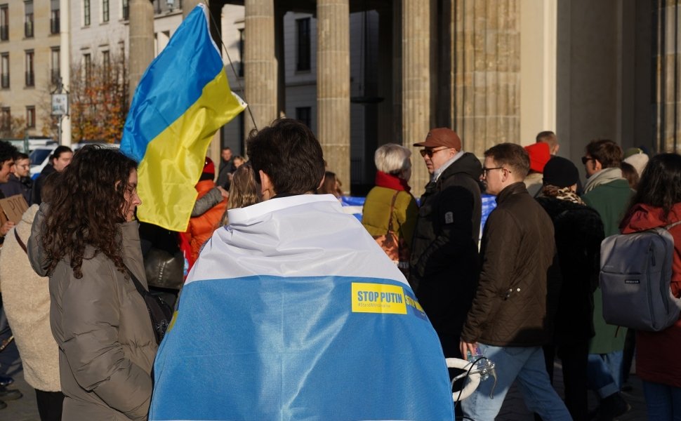 Berlin, Germany - November 13, 2022: Male demonstrator covered with a white-blue-white flag at a rally in solidarity with Ukraine against Russian Imperialism at Brandenburg Gate in Berlin