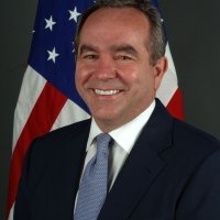 A headshot of Kurt Campbell standing in front of an American flag