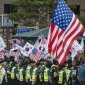 A crowd of people are waving U.S. and South Korean flags, standing behind a line of policemen.